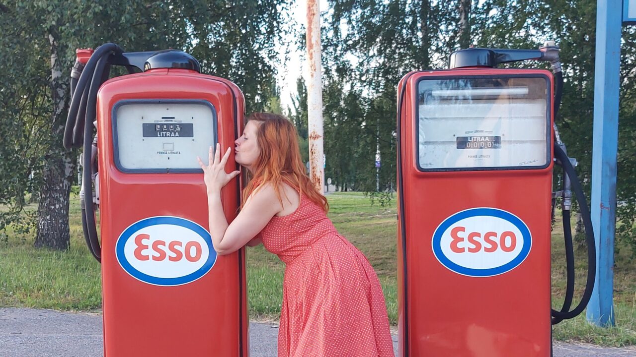 Nainen suutelee bensatankkia kesämekko päällänsä.