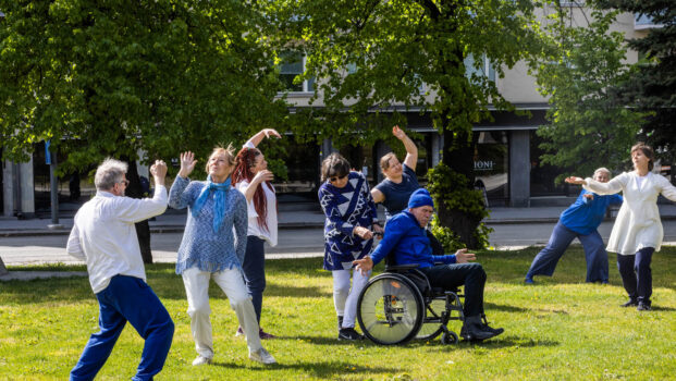 Kuvassa on aikuisia ihmisiä tanssimassa ulkona nurmikolla kesällä. Yksi on pyörätuolissa.