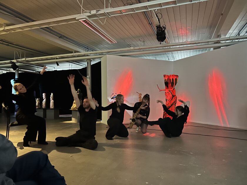 Saksofonisti ja neljä tanssojaa esiintymässä taidegalleriassa.