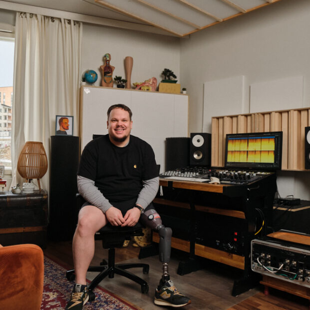 Kuvassa Janne Hakanen, palveluntarjoaja. Istuu studiolaitteiston edessä ja hymyilee.