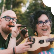 Kuvassa Palago-yhtyeen jäsenet Iago ja Paloma poseeraavat monien soittimien kanssa. Iago puhaltaa huiluun ja pitelee marakasseja, Palomalla on edessään ukulele-kitara. Taustalla näkyy puita ja hiukan valoisaa taivasta. Tunnelma on energinen ja innostunut. Kuvan vasemmassa yläkulmassa on värikkäitä pisarakuvioita ja oikeassa yläkulmassa Uulun vaaleanpunainen logo valkoisen pilvikuvion päällä.