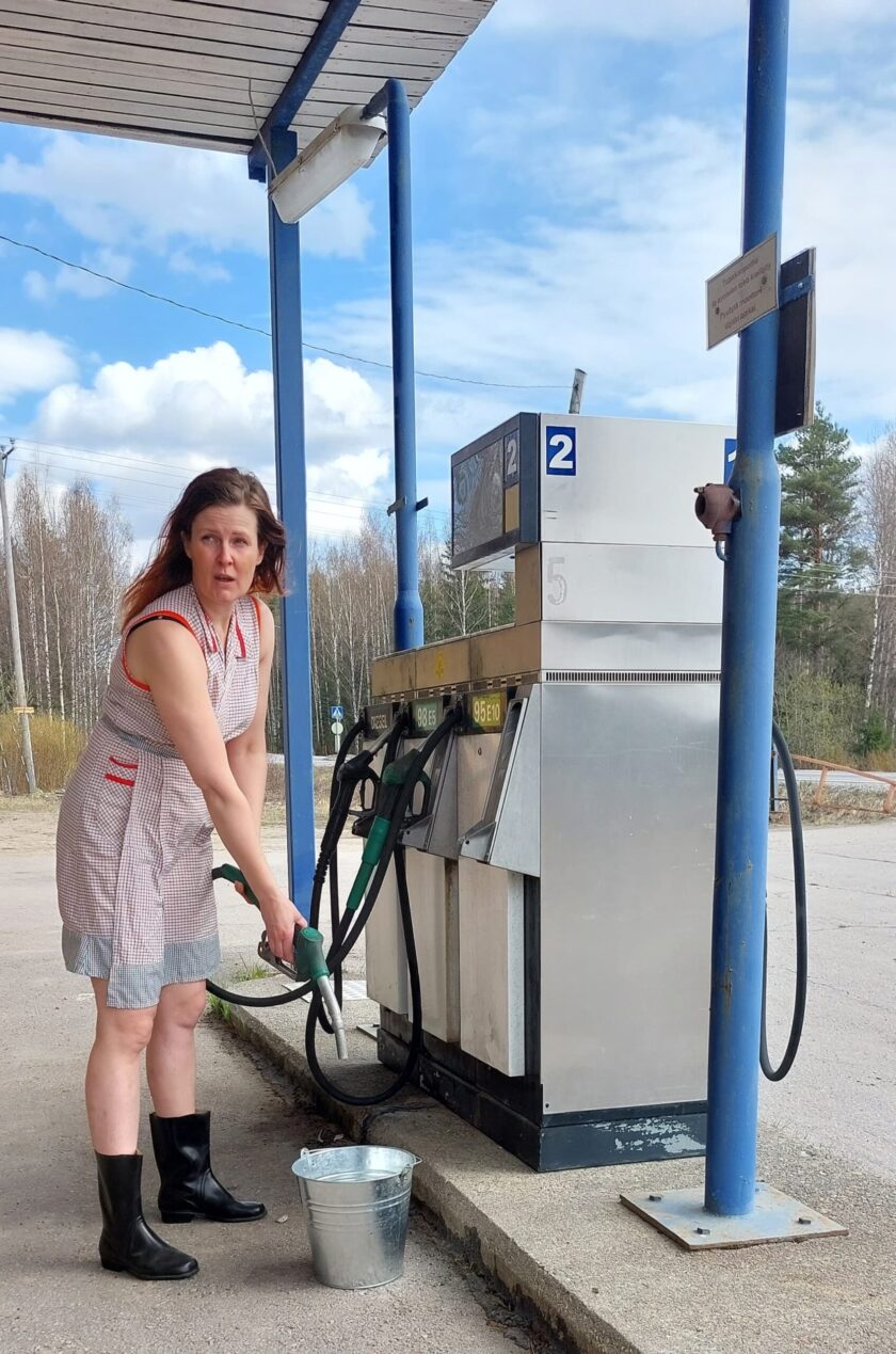Nainen tankkaa bensaa ämpäriin huoltoasemalla.