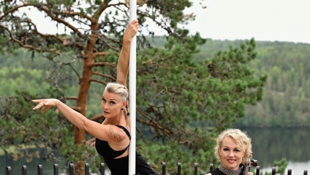 Tankoleidit suomalaisessa kulttuurimaisemassa, Hämeenlinnan Aulangon näköalatasanteella. Elina soittaa selloa, Tintti tanssii tangolla. Taustalla uljas mänty, näköalatasanteen kaunis musta metallikaide ja järvi, jonka takana siintää metsää.