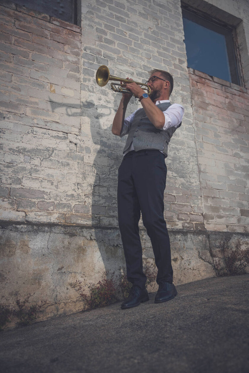 Fredrik Erlandsson står framför en tegelvägg och spelar trumpet.